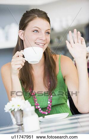 Stock Image - Young woman sitting at a table drinking tea. Fotosearch