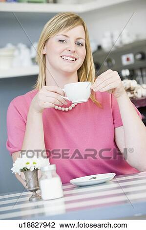 Young woman sitting at a table drinking tea View Large Photo Image Stock Image - Young woman sitting at a table drinking tea. Fotosearch