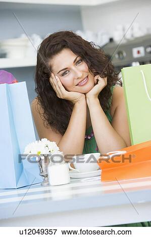 Young woman sitting at a table taking a break from shopping and drinking tea View Large Photo Image Stock Photo - Young woman sitting at a table taking a break from shopping and drinking tea. Fotosearch