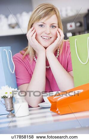 Young woman sitting at a table taking a break from shopping View Large Photo Image Stock Photo - Young woman sitting at a table taking a break from shopping. Fotosearch