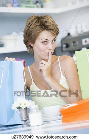 Stock Photo - Young woman sitting at a table taking a break from shopping and drinking tea. Fotosearch