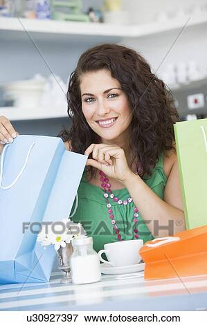 Stock Photo - Young woman sitting at a table taking a break from shopping and drinking tea. Fotosearch