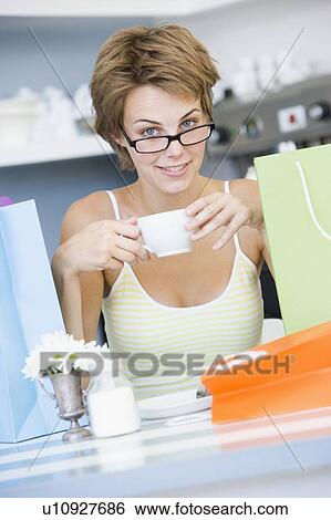 Stock Photograph - Young woman sitting at a table taking a break from shopping and drinking tea. Fotosearch