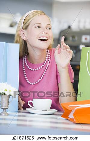 Stock Photography - Young woman sitting at a table taking a break from shopping and drinking tea. Fotosearch