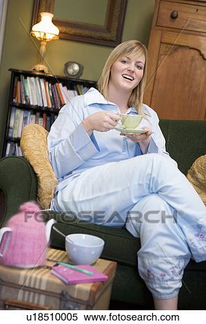 Stock Photography - Young woman sitting on sofa at home drinking tea. Fotosearch
