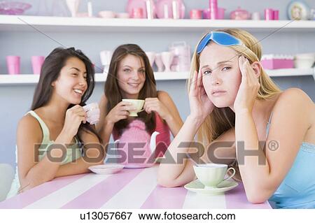 Stock Photo - Young woman with a hangover sitting at a table with two friends. Fotosearch