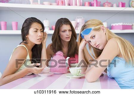 Stock Photograph - Young woman with a hangover sitting at a table with two friends. Fotosearch