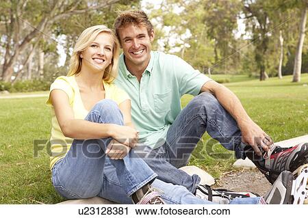 Stock Image - Couple Putting On In Line Skates In Park. Fotosearch