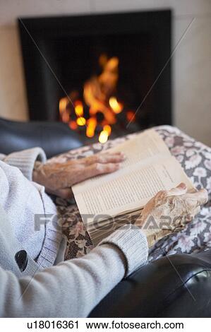Stock Image - Detail Of Senior Woman Reading Book By Fire At Home. Fotosearch