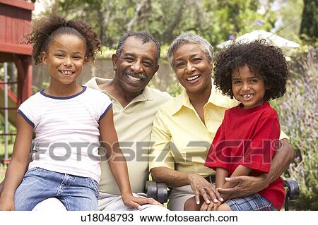 Stock Image - Grandparents Relaxing In Garden With Grandchildren. Fotosearch