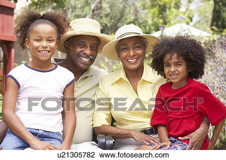Stock Image - Grandparents Relaxing In Garden With Grandchildren. Fotosearch