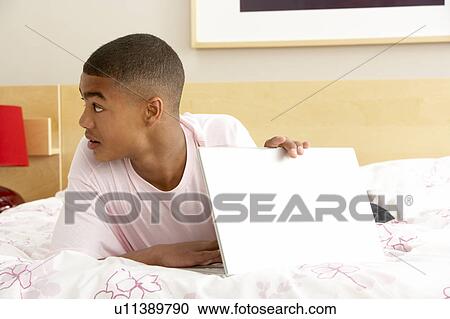 Stock Image - Guilty Teenage Boy Using Laptop In Bedroom. Fotosearch