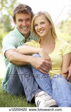 Stock Image - Portrait Of Young Couple Sitting In Park. Fotosearch