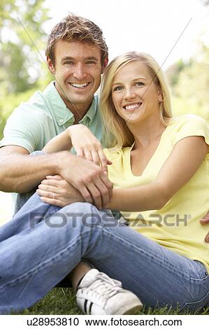 Stock Image - Portrait Of Young Couple Sitting In Park. Fotosearch