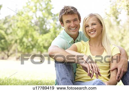 Stock Photo - Portrait Of Young Couple Sitting In Park. Fotosearch