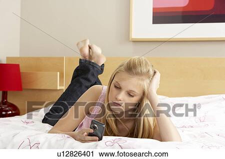 Stock Image - Sad Teenage Girl In Bedroom With Mobile Phone. Fotosearch