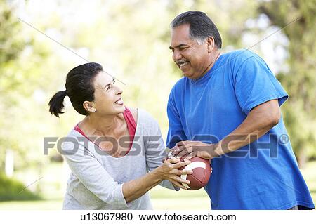 Stock Image - Senior Couple Exercising With American Football In Park. Fotosearch