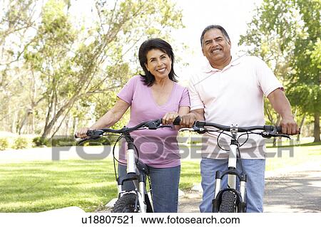 Stock Image - Senior Couple Riding Bikes In Park. Fotosearch