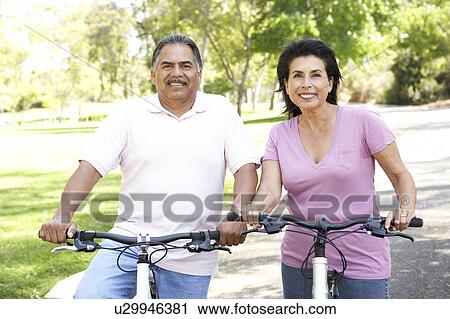 Stock Image - Senior Couple Riding Bikes In Park. Fotosearch