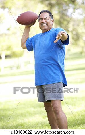 Stock Image - Senior Man Exercising With American Football In Park. Fotosearch
