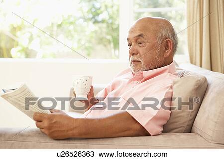 Stock Image - Senior Man Reading Book With Drink At Home. Fotosearch