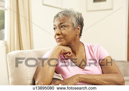 Stock Image - Senior Woman Looking Thoughtful In Chair At Home. Fotosearch