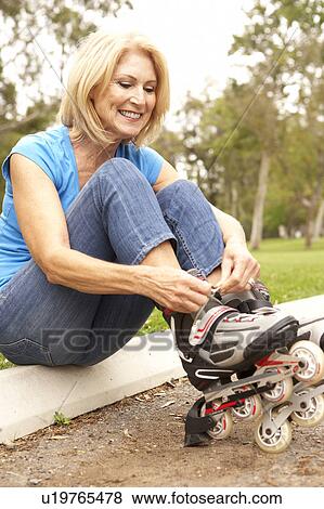 Stock Photo - Senior Woman Putting On In Line Skates In Park. Fotosearch