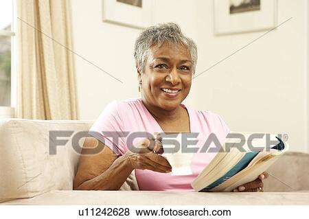 Stock Photo - Senior Woman Reading Book With Drink At Home. Fotosearch