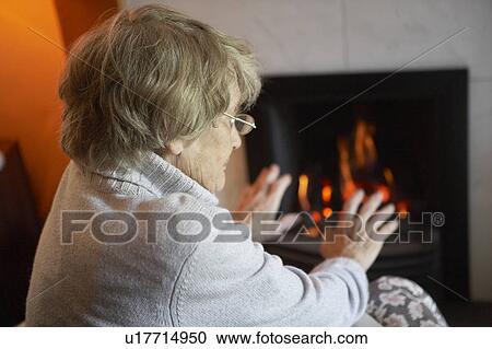 Stock Image - Senior Woman Warming Hands By Fire At Home. Fotosearch