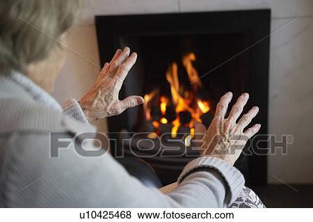 Senior Woman Warming Hands By Fire At Home View Large Photo Image Stock Photo - Senior Woman Warming Hands By Fire At Home. Fotosearch