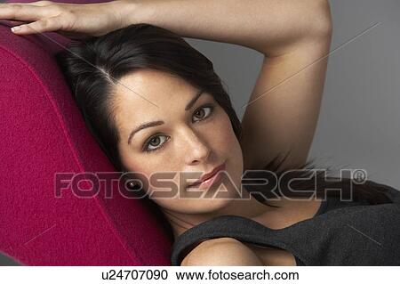 Stock Image - Studio Portrait Of Woman Relaxing On Pink Chaise Longue. Fotosearch