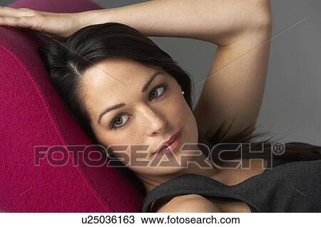 Stock Image - Studio Portrait Of Woman Relaxing On Pink Chaise Longue. Fotosearch