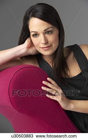 Stock Image - Studio Portrait Of Woman Relaxing On Pink Chaise Longue. Fotosearch