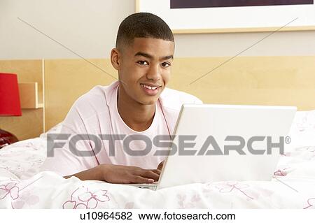 Stock Image - Teenage Boy Using Laptop In Bedroom. Fotosearch