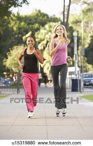 Stock Image - Two Female Friends Jogging On Street. Fotosearch
