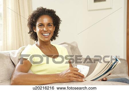 Stock Photograph - Woman Reading Book With Drink At Home. Fotosearch