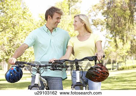 Stock Image - Young Couple On Cycle Ride in Park. Fotosearch