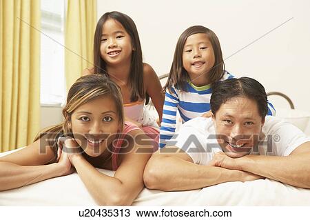 Stock Image - Young Family Relaxing In Bedroom. Fotosearch
