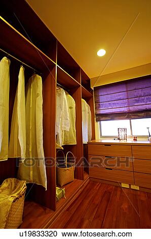 Stock Image - Closet with clothes in protective wrapping hanging in it, and drawers by the window. Fotosearch