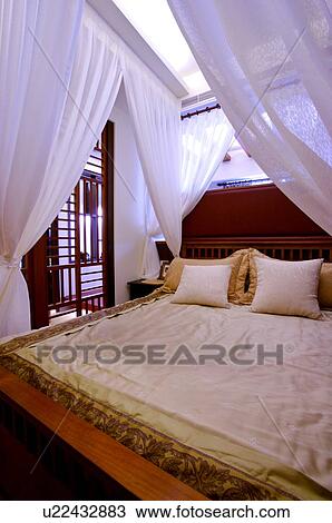 Stock Image - Luxurious four poster bed, with white curtains tied up at the four corners. Fotosearch