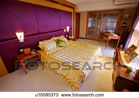 Stock Image - Modern bedroom with a made bed, desk, and furniture. Fotosearch