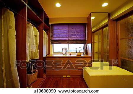Stock Image - Modern dressing room with clothes hanging on one side, drawers, and a long mirror. Fotosearch