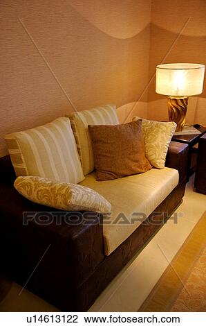 Stock Image - Sofa with cushions on it, next to a small table with a lamp. Fotosearch
