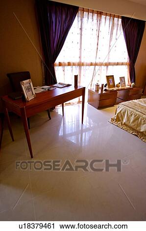 Stock Image - Wooden desk with a photo frame and books on it next to a window, in a bedroom. Fotosearch