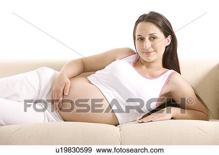 Stock Photo - Pregnant woman lying on her side on a sofa, one hand on her abdomen. Fotosearch