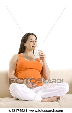 Stock Image - Pregnant young woman holding a milk bottle, sitting cross-legged. Fotosearch