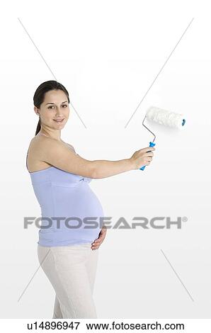 Pregnant young woman holding a paint roller, smiling View Large Photo Image Stock Photo - Pregnant young woman holding a paint roller, smiling. Fotosearch
