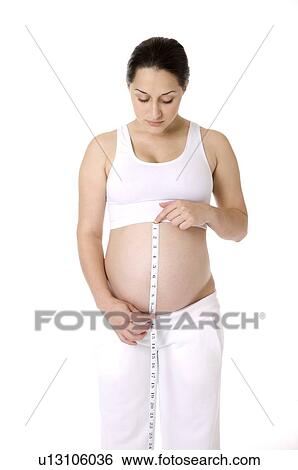 Pregnant young woman holding a tape measure, measuring her abdomen View Large Photo Image Stock Photograph - Pregnant young woman holding a tape measure, measuring her abdomen. Fotosearch