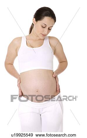Stock Photo - Pregnant young woman looking down, hands on her stomach. Fotosearch