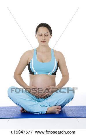 Stock Photo - Pregnant young woman sitting cross legged on map, eyes closed. Fotosearch